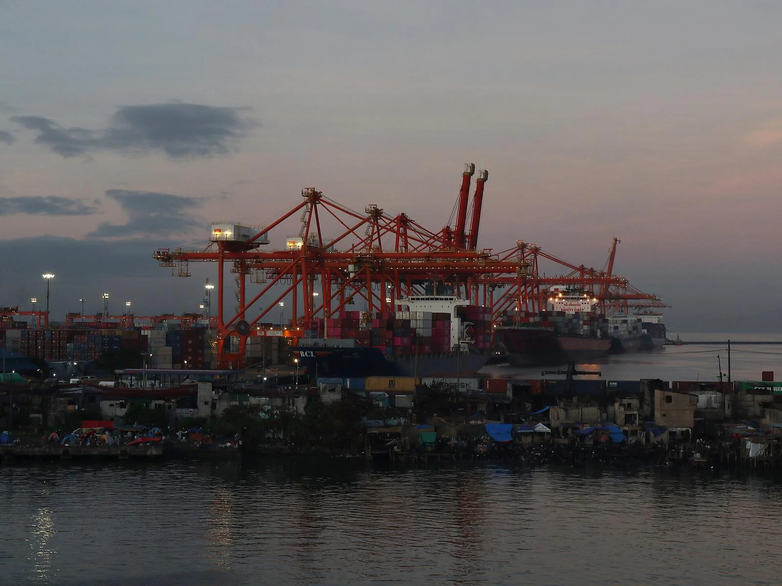 Orange gantry cranes loading container ships at the Manila International Container Terminal at dusk