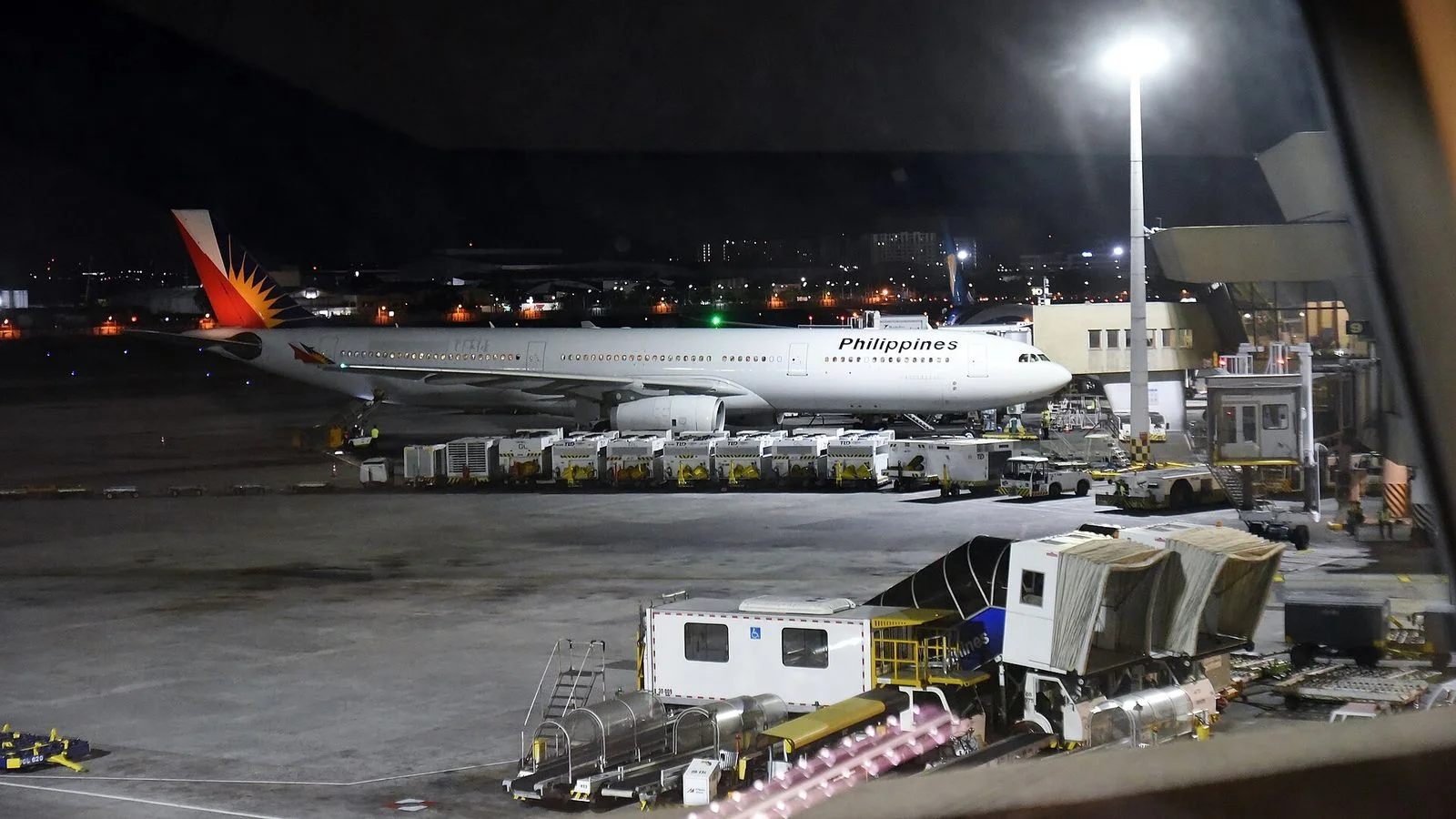 Philippine Airlines Airbus A330 parked at a gate at Ninoy Aquino International Airport at night, with airport service vehicles in front