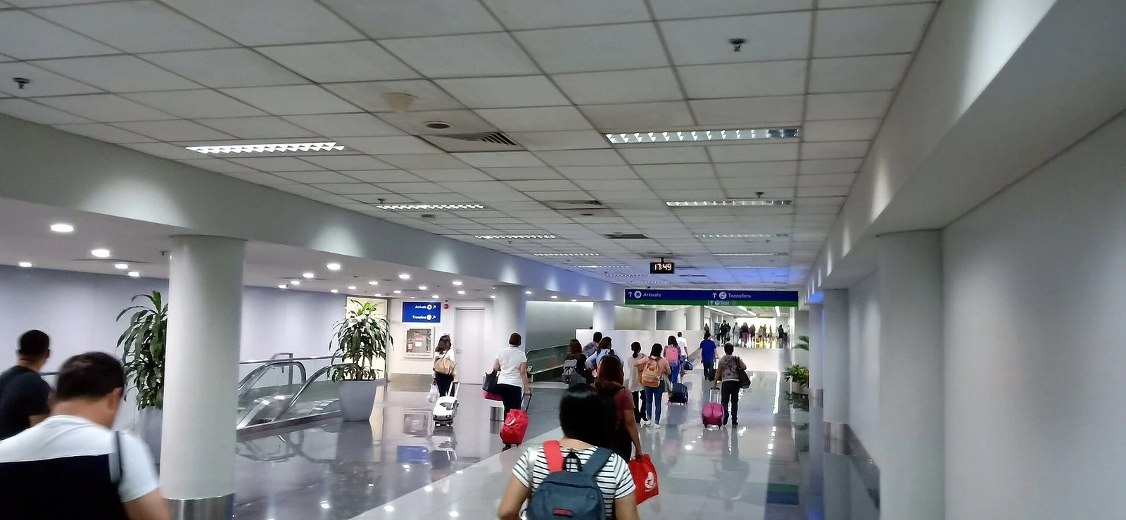 Passengers with luggage walking toward the Arrivals and Transfers signs inside NAIA Terminal 3