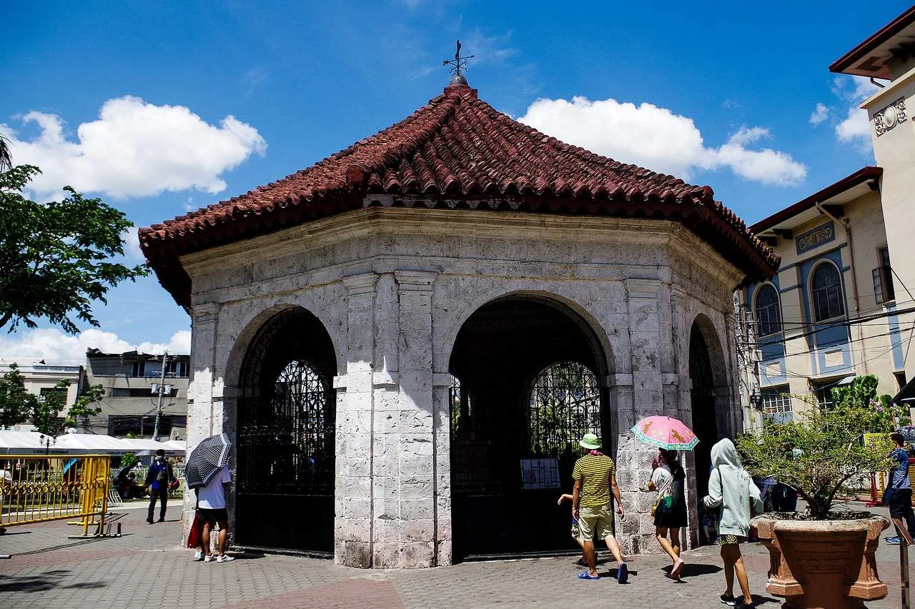 The octagonal kiosk of Magellan's Cross in Cebu City with visitors under umbrellas