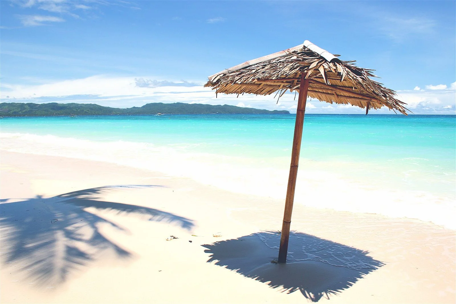 A thatched beach umbrella on the white sand of Boracay's White Beach with turquoise water behind
