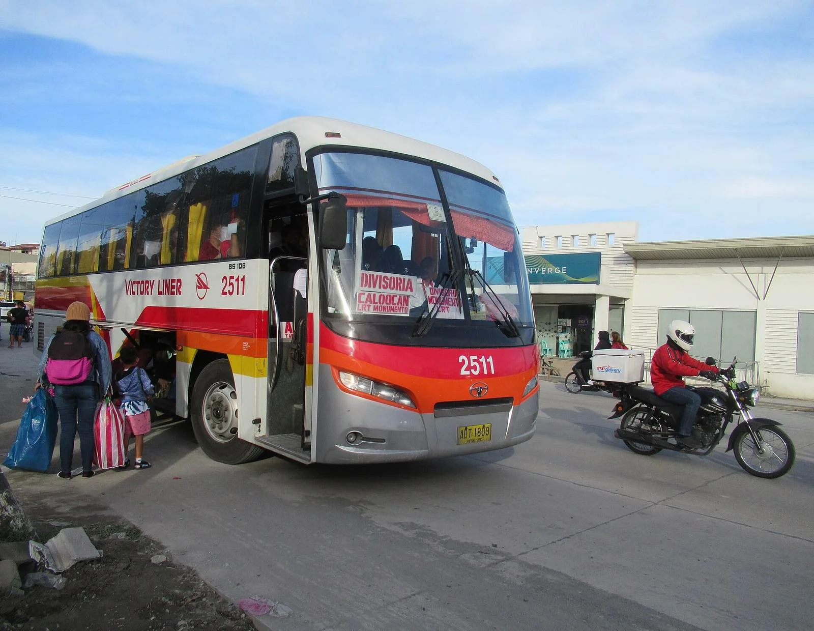 A red and white Victory Liner bus picking up passengers with bags at the roadside
