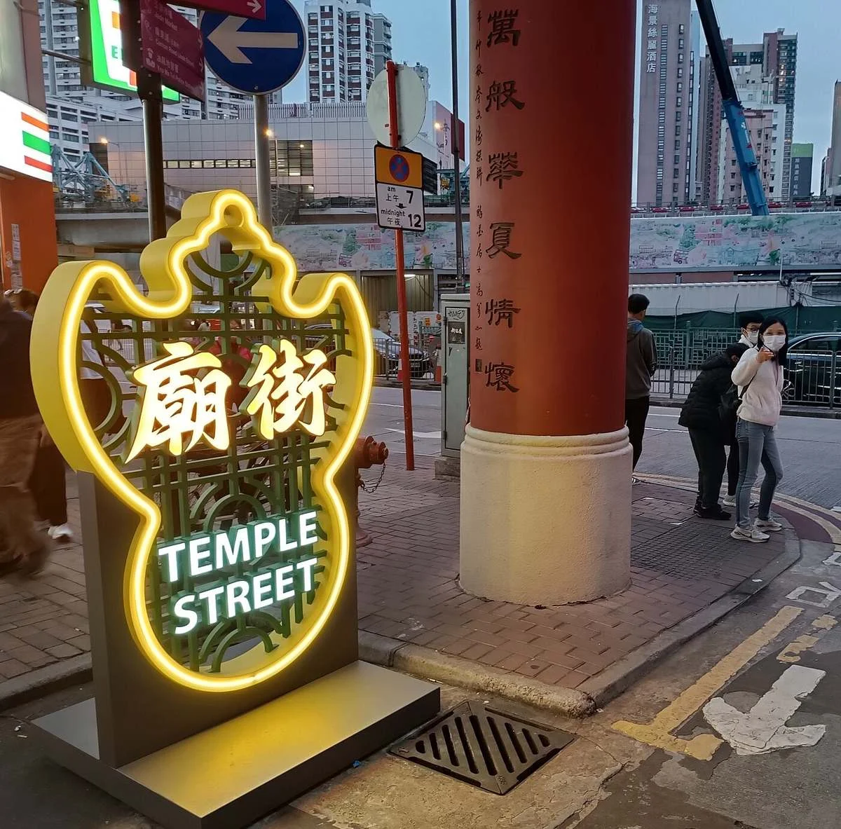 Lit neon Temple Street sign at the entrance to the Yau Ma Tei night market at dusk