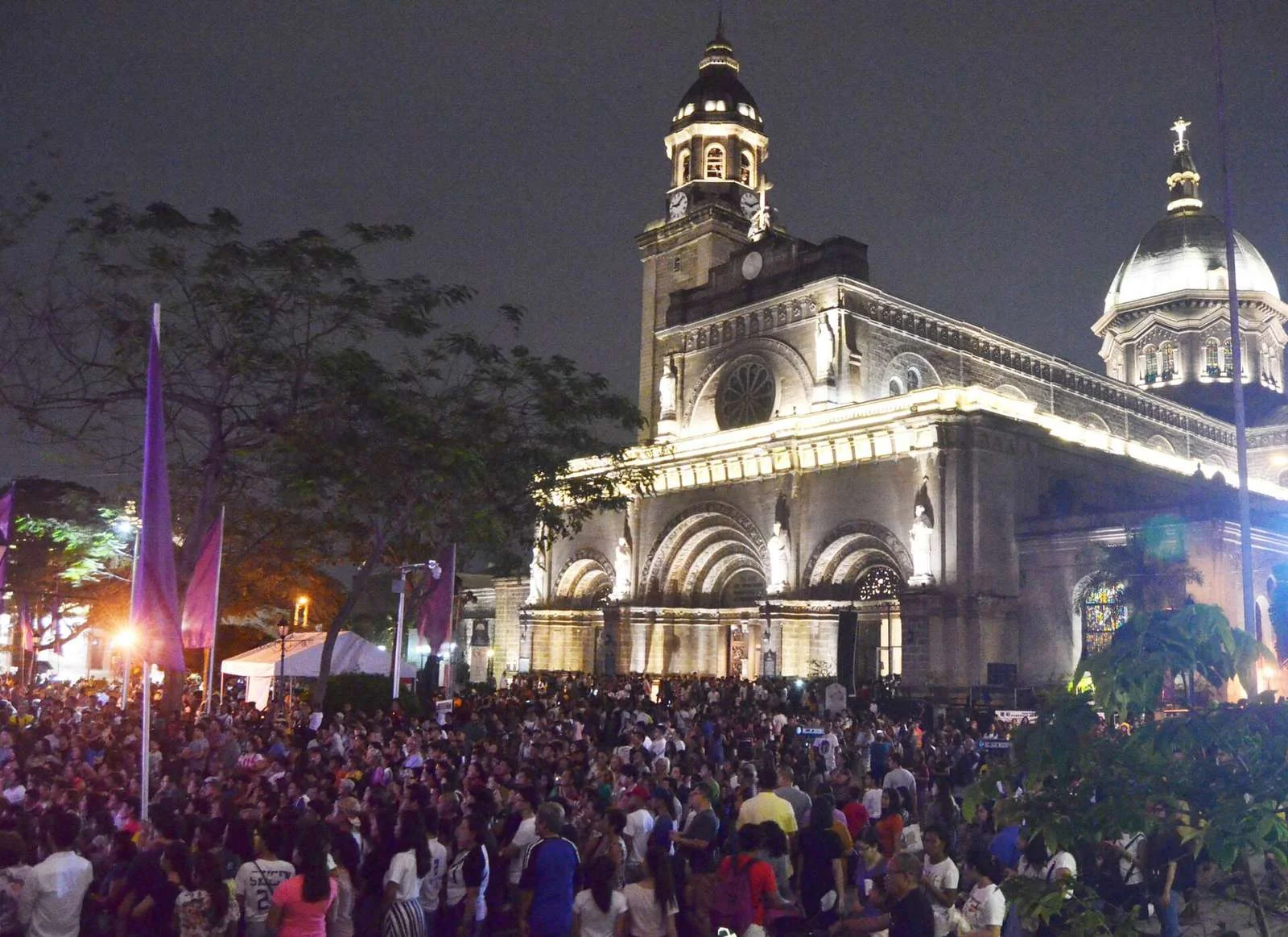 Crowds outside the lit facade of the Manila Cathedral at night during Holy Week
