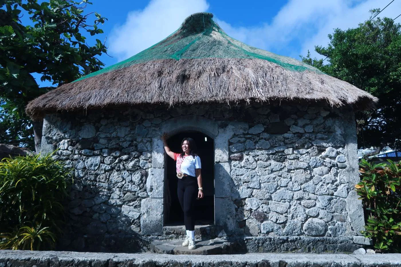 Thatched roof Ivatan stone house in Batanes with a woman standing in the doorway