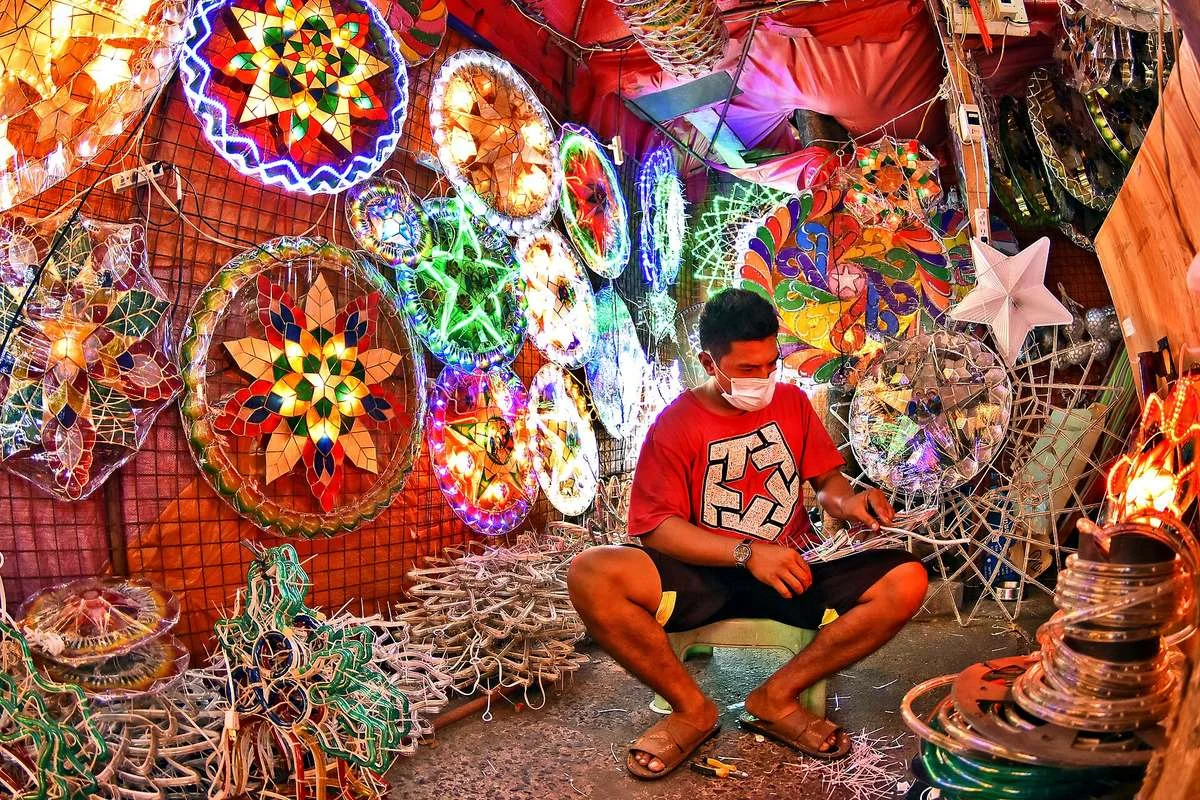Parol maker surrounded by colourful Christmas lanterns in his workshop