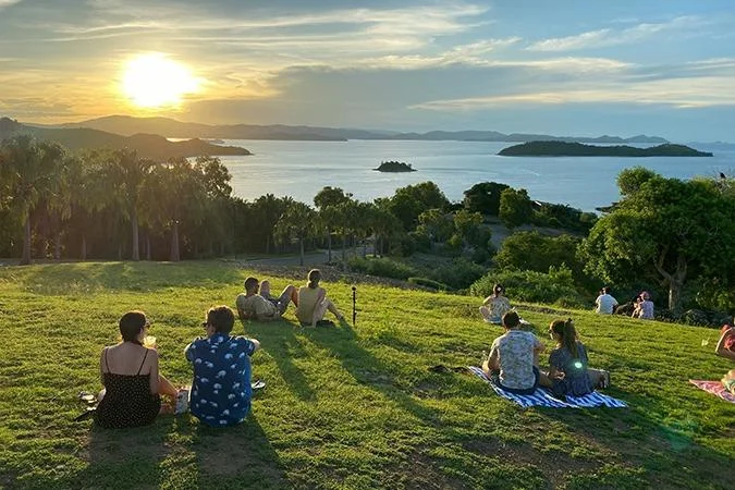 Visitors watching the sunset from the grass at One Tree Hill, looking west across the Whitsunday islands